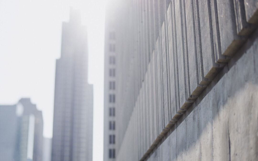 Low-angle view of a concrete wall with blurred skyscrapers in the background, under bright sunlight.